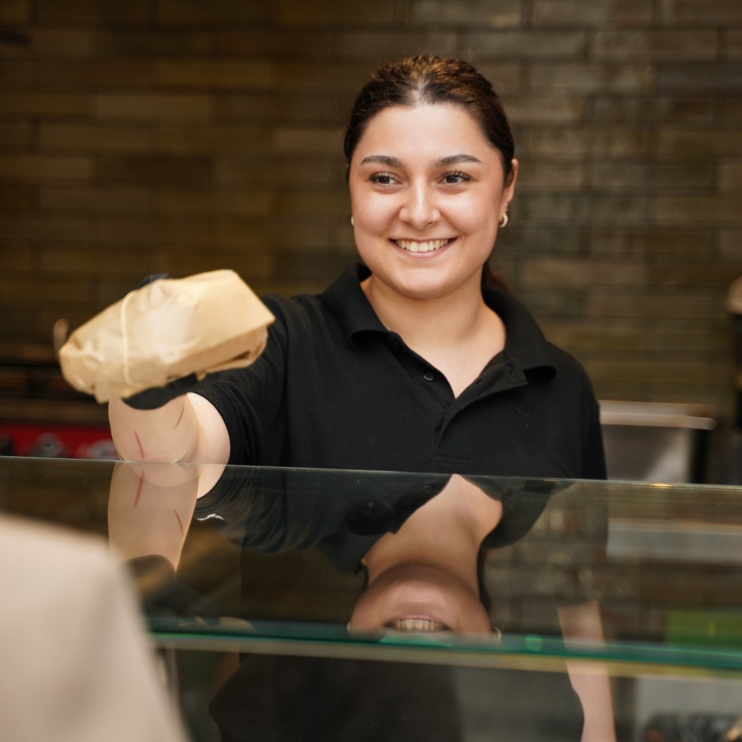 Smilende medarbejder fra Wilhelm Deli i Randers giver kunde sandwich.